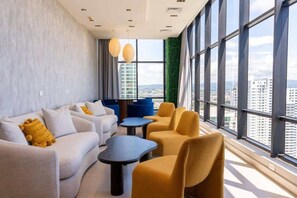 A modern lounge with a sofa set, armchairs, and a coffee table, large windows with a city view, and a green accent wall. - Serviced Studio with City & Ocean View in Panama U902 (Panamá)