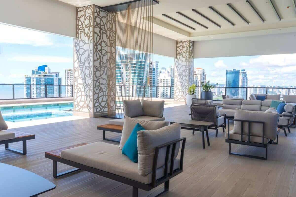 A modern lounge area with a pool view, contemporary furniture, and a cityscape in the background.
