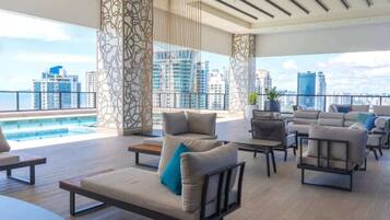 Un área de descanso moderna con vista a la piscina, muebles contemporáneos y un paisaje urbano de fondo.