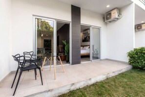 Eine moderne Terrasse mit Gartenmöbeln aus Glas, ein Bett ist durch die Schiebetür erkennbar, und ein kleiner Gartenbereich.