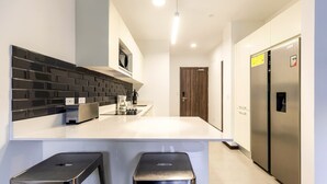 Cozinha moderna com bancada branca, painel de fundo preto, eletrodomésticos de aço inoxidável e dois bancos pretos.