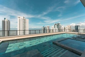 Une piscine sur le toit offrant une vue panoramique sur la ville, entourée d’immeubles de grande hauteur.