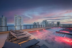 Ein Pool auf dem Dach mit Liegestühlen und Blick auf den Stadt-Horizont.