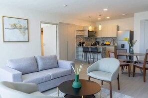 Un salon moderne avec un canapé, des fauteuils, une table basse et une cuisine en arrière-plan.