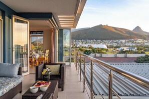 A balcony with a view of a city and a mountain. There is a dining area with a table and chairs, and a sofa with a tray of snacks. - Perfect Views, Sleeps 6, Mouille Point - Emerald Horizon (Cape Town)