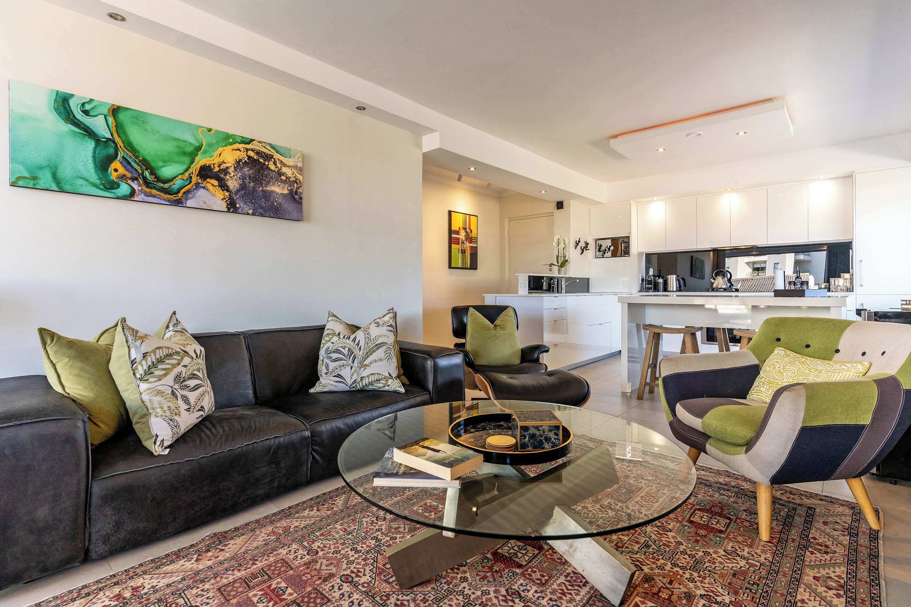 Una sala de estar moderna con una mesa de centro de vidrio, sofá de cuero y una alfombra estampada.