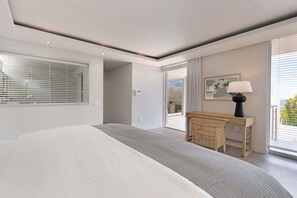A modern hotel room with a large bed, a desk, and a view of the outdoors through the window. - Family Villa, Pool, Ocean Views - Camps Bay Grace (Cape Town)