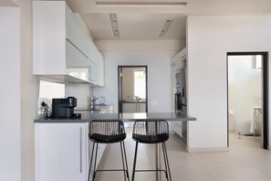 A modern kitchen with white cabinetry, a black countertop, and two black bar stools. - Family Villa, Pool, Ocean Views - Camps Bay Grace (Cape Town)