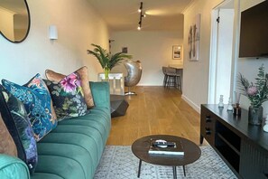 Ein Wohnzimmer mit einem grünen Sofa, einem Couchtisch und einem Essbereich im Hintergrund.