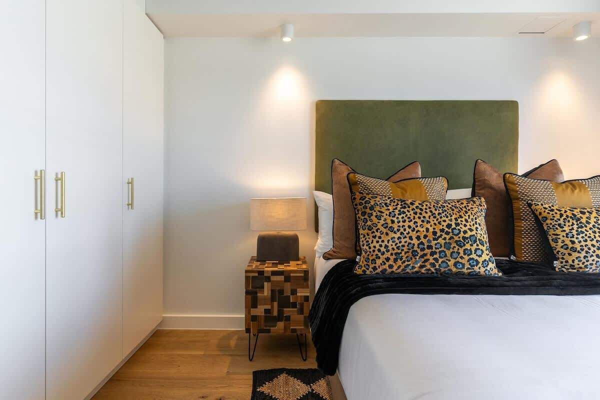 A bedroom with a bed, pillows, a nightstand, and a wall-mounted lamp.