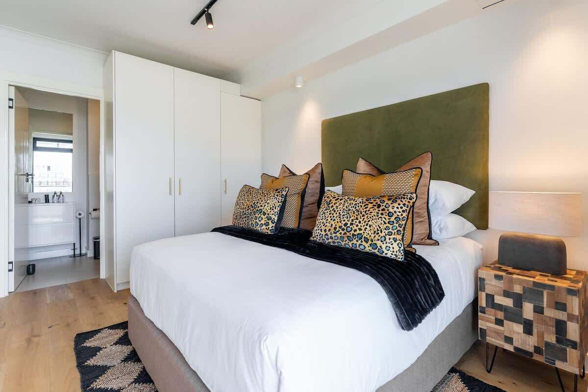 A modern bedroom with a large bed, a headboard, and a bedside table with a lamp.