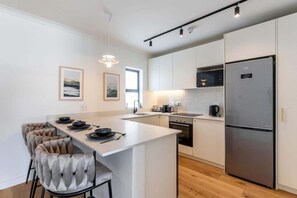 A modern kitchen with white cabinetry, a central island, and a stainless steel refrigerator. - Location, Luxury, Sea Point, Views -Topaz Views Apt (Cape Town)