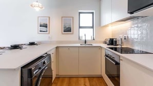 A modern kitchen with white cabinetry, a built-in dishwasher, and a large window providing natural light. - Location, Luxury, Sea Point, Views -Topaz Views Apt (Cape Town)