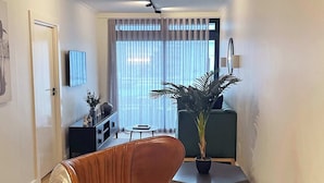 A modern living room with a sofa, a dining table, a potted plant, and a TV mounted on the wall. - Location, Luxury, Sea Point, Views -Topaz Views Apt (Cape Town)