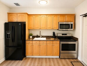 Una cucina con mobili in legno, un frigorifero nero, un forno in acciaio inossidabile e un microonde.
