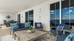 Ein geräumiger Balkon mit einem Holztisch, blauen Polster-Sofa und einem großen Fenster mit Blick zum Himmel.