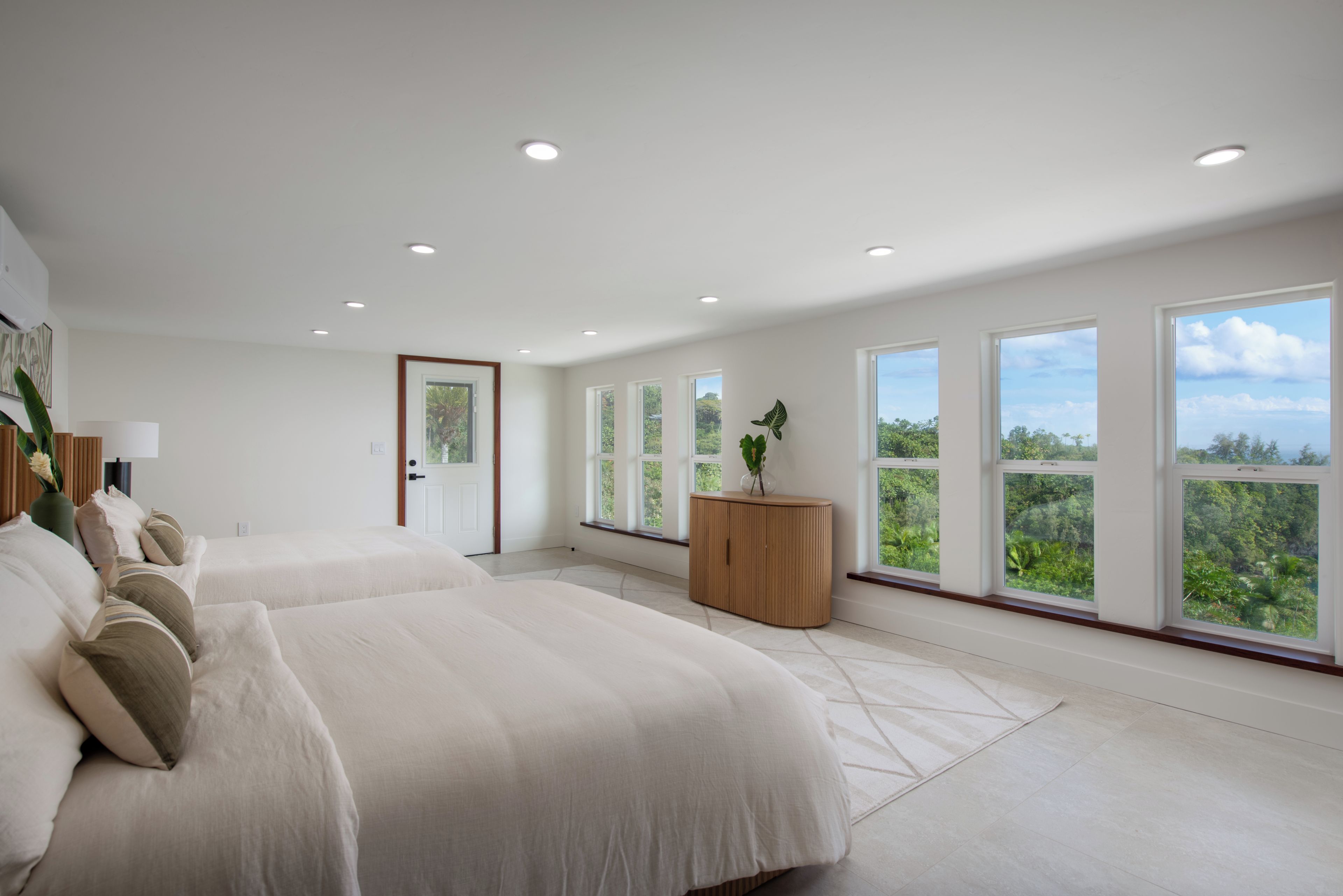 A spacious bedroom with two beds, large windows, and a view of greenery.