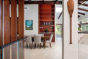 A modern dining area with a wooden table and chairs, a wooden shelf with glassware, and a wooden paddle on the wall. - Onomea Oasis (Papaikou)