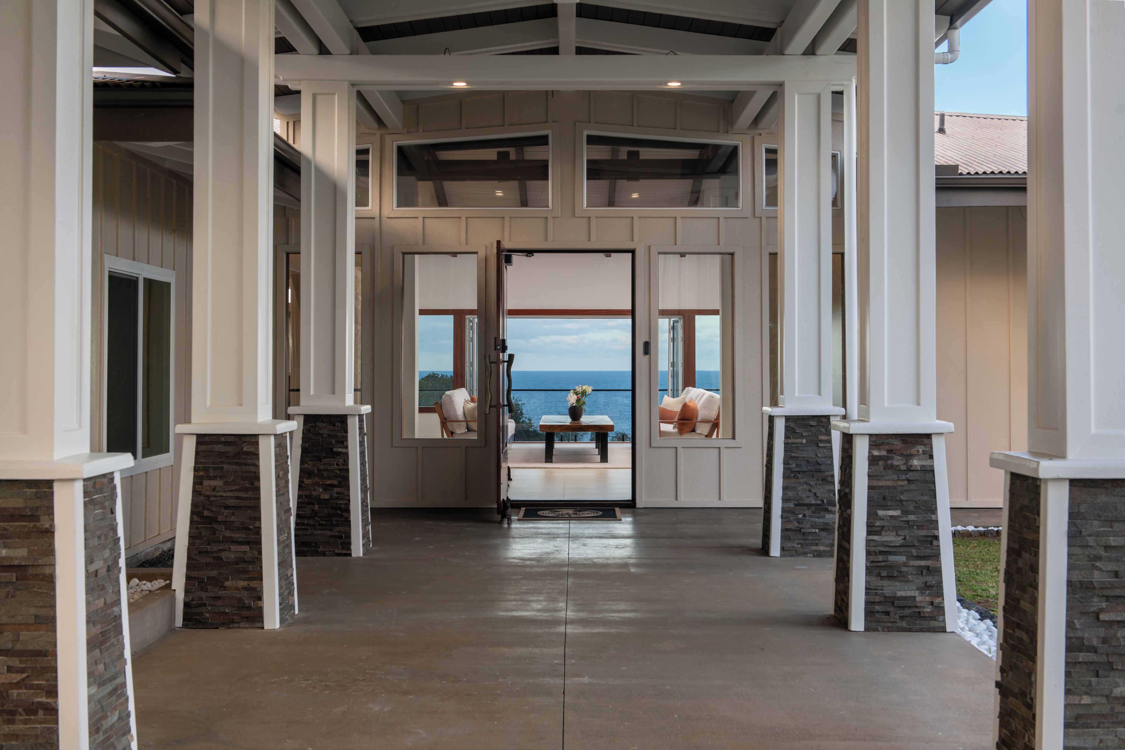 A covered outdoor area with stone pillars, a view of the ocean, and a seating area with a table and chairs.