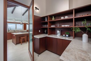 A modern kitchen with wooden cabinets, a marble countertop, and a view of the ocean. - Onomea Oasis (Papaikou)