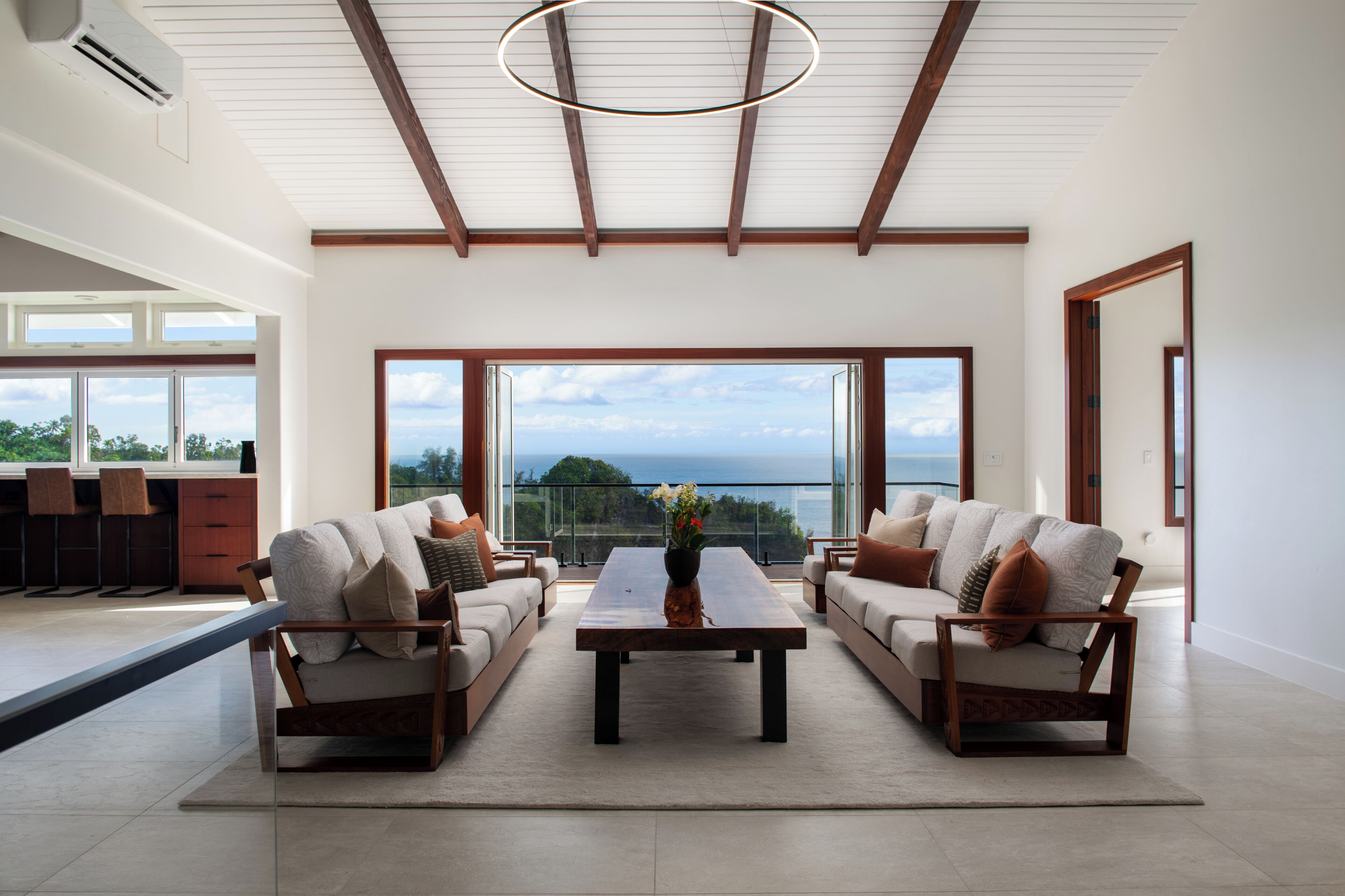 A spacious living area with a large window offering a view of the ocean, a modern ceiling design, and a minimalist furniture arrangement.