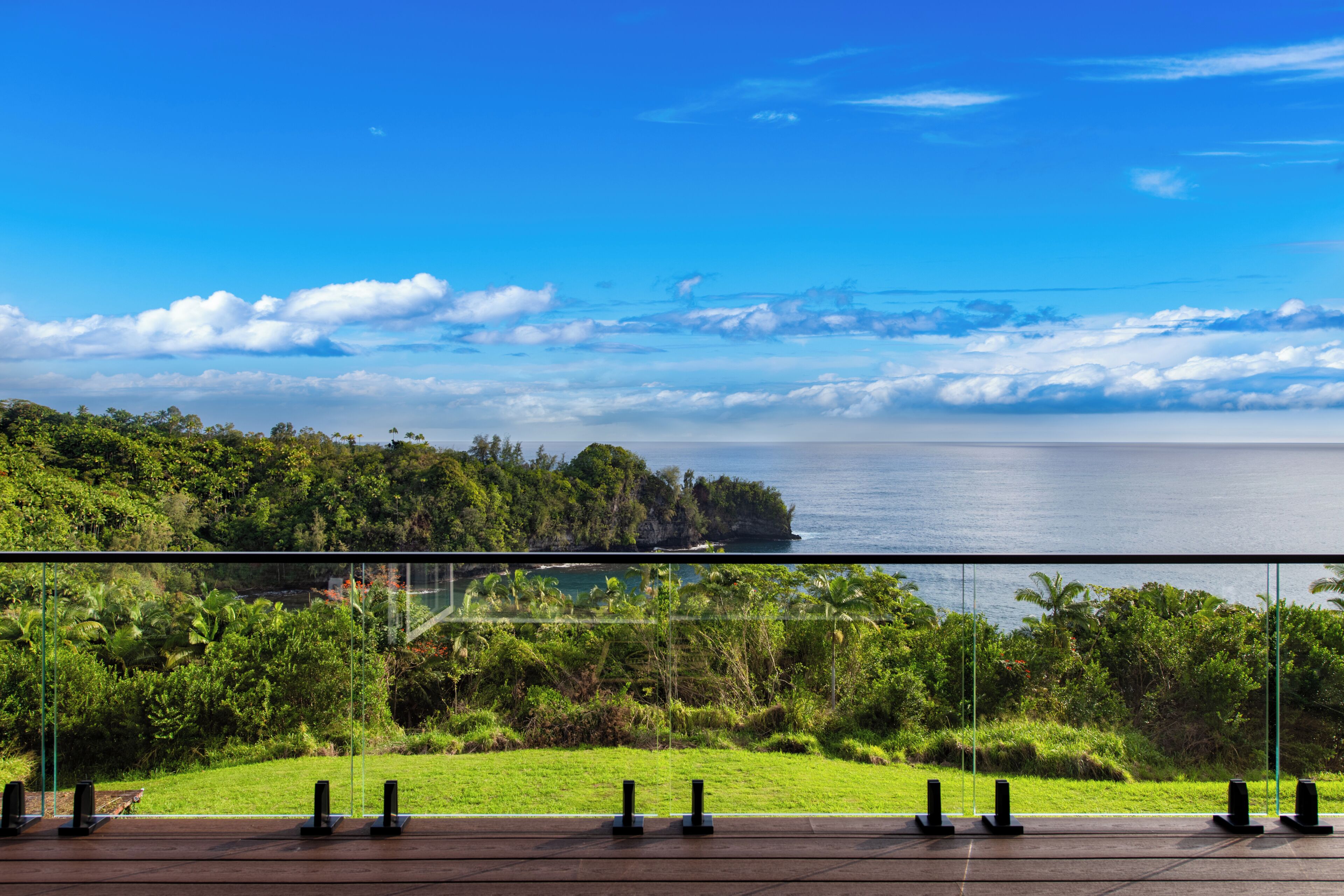A balcony with a clear view of the ocean and lush greenery.