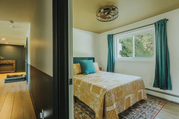 Une chambre à coucher avec un lit, une fenêtre avec des rideaux, un ventilateur de plafond et une cheminée.