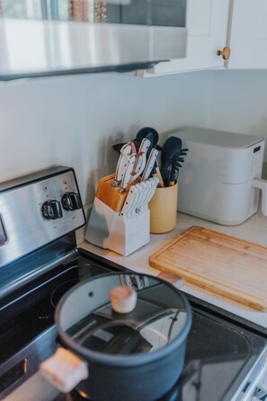Une cuisine équipée d’une cuisinière, d’une casserole, d’une planche à découper, d’un porte-couteaux et d’un four à micro-ondes.