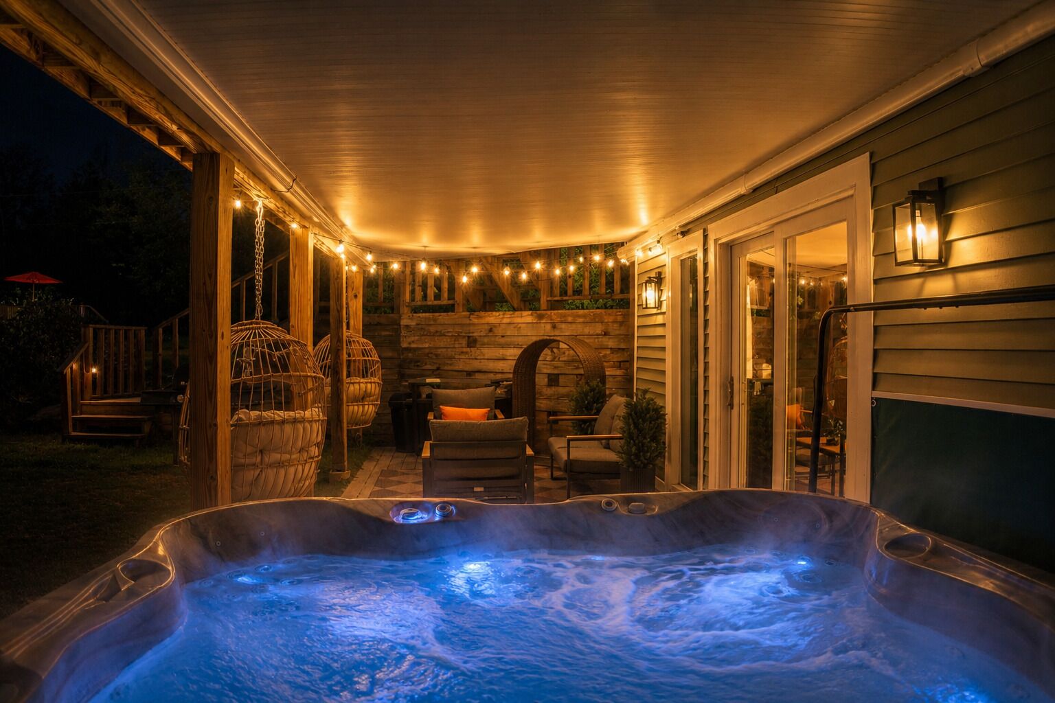 Un bain à remous avec une terrasse en bois, des guirlandes lumineuses et du mobilier d’extérieur.