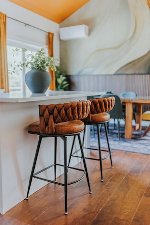 Eine Bar mit zwei gepolsterten Barhocker, einem Topf mit Pflanze und einem Holztisch.