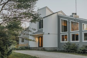 Una casa moderna de dos pisos con techo inclinado, ventanas grandes y una chimenea visible.