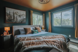 Quarto com uma cama grande, duas mesas de cabeceira, um quadro na parede e uma janela com cortinas.