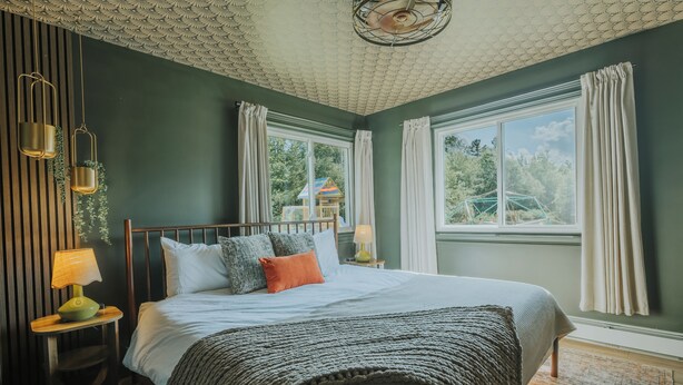 Un dormitorio con cama, mesita de noche, lámpara y ventana con cortinas.