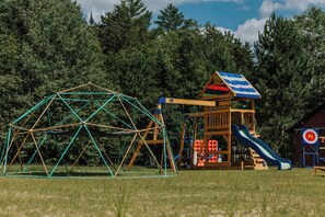 Une aire de jeux avec une structure d’escalade en forme de dôme, un toboggan et une balançoire.