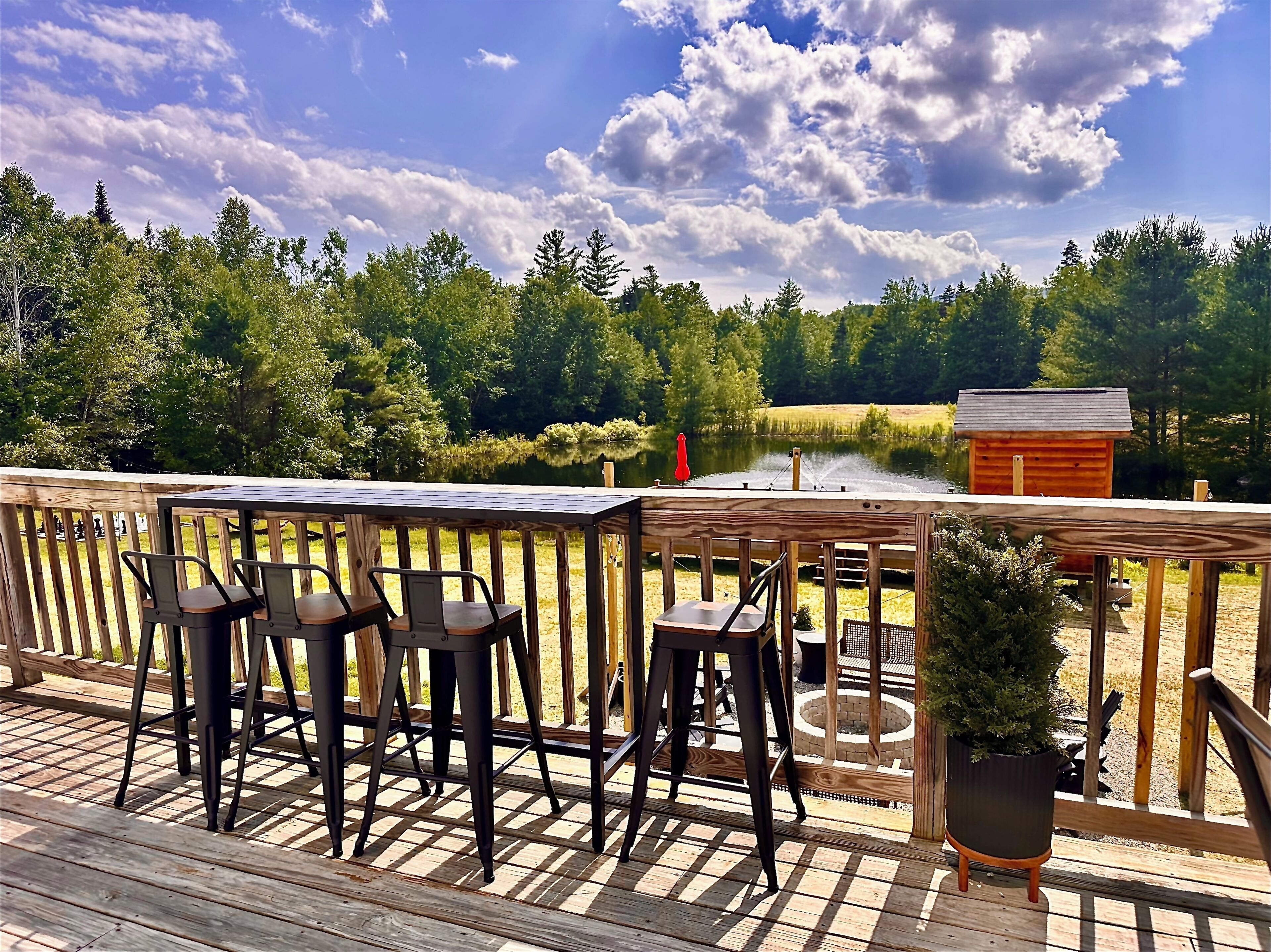 A wooden deck with a table and chairs, overlooking a lake and surrounded by trees.