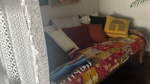 Ein Zimmer mit einem Bett, einem Bild an der Wand, einer Topfpflanze und einem Spitzenvorhang.