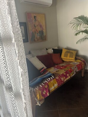 Ein Zimmer mit einem Bett, einem Bild an der Wand, einer Topfpflanze und einem Spitzenvorhang.