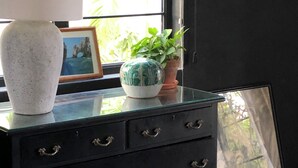 Ein schwarzer Kommode mit Glasplatte, eine weiße Vase, eine grüne Pflanze und ein gerahmtes Bild.