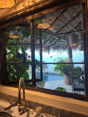 A window with a view of a pool and outdoor seating area, surrounded by lush greenery and a thatched roof structure. - Los Cabos Retreat
3/3 home, 24 Hr. security, private pool gated compound (San José del Cabo)