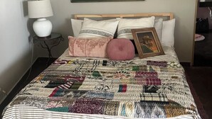 Ein Bett mit einem gemusterten Quilt, einer Nachttischlampe und einem gerahmten Kunstwerk an der Wand.