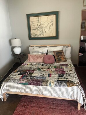 Ein Bett mit einem gemusterten Quilt, einer Nachttischlampe und einem gerahmten Kunstwerk an der Wand.
