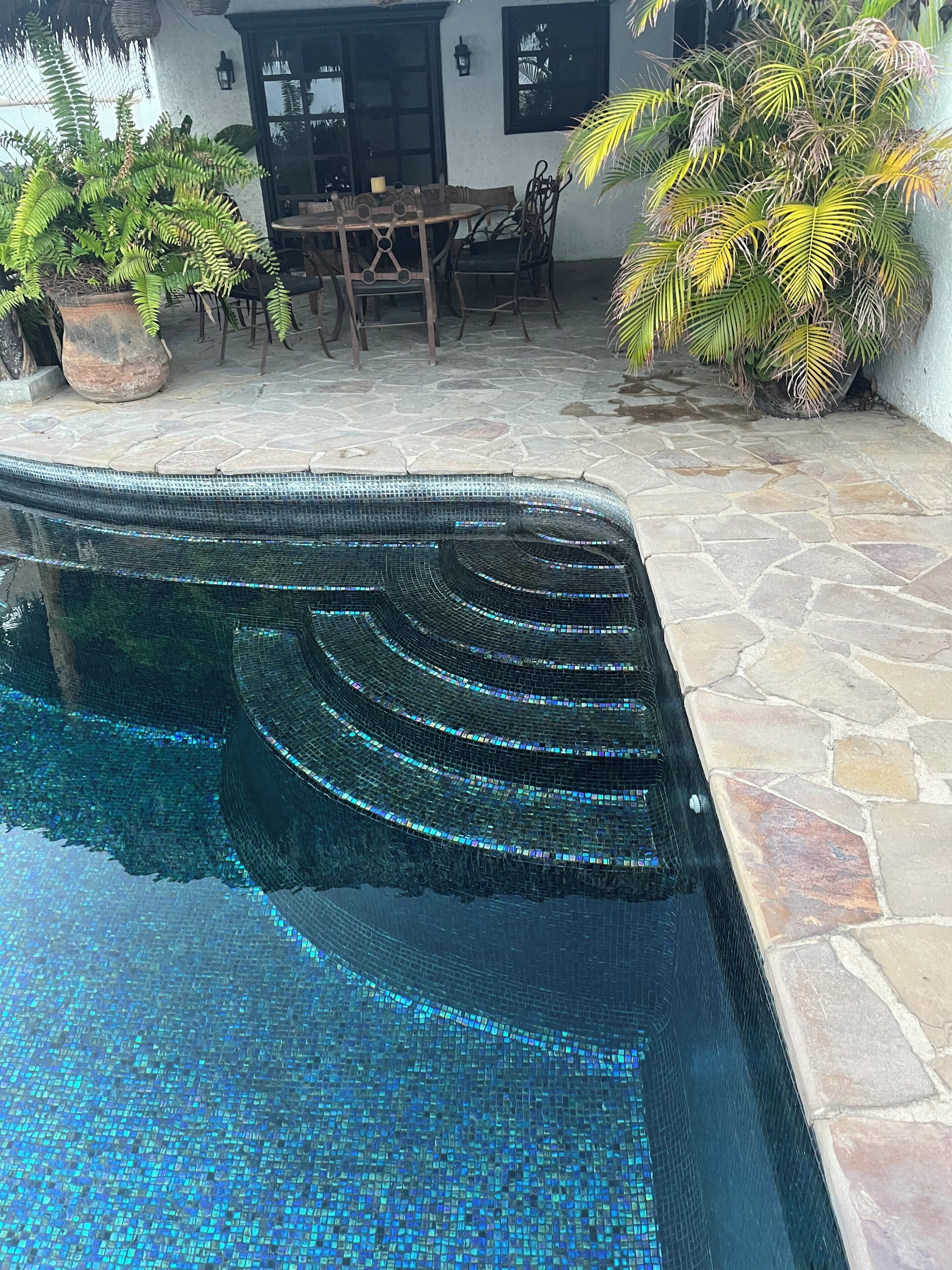 A swimming pool with mosaic tiles, surrounded by stone flooring and potted plants.