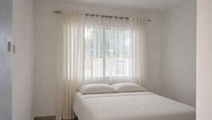 Una habitación con una cama, un ventanal con cortinas ligeras y una puerta.