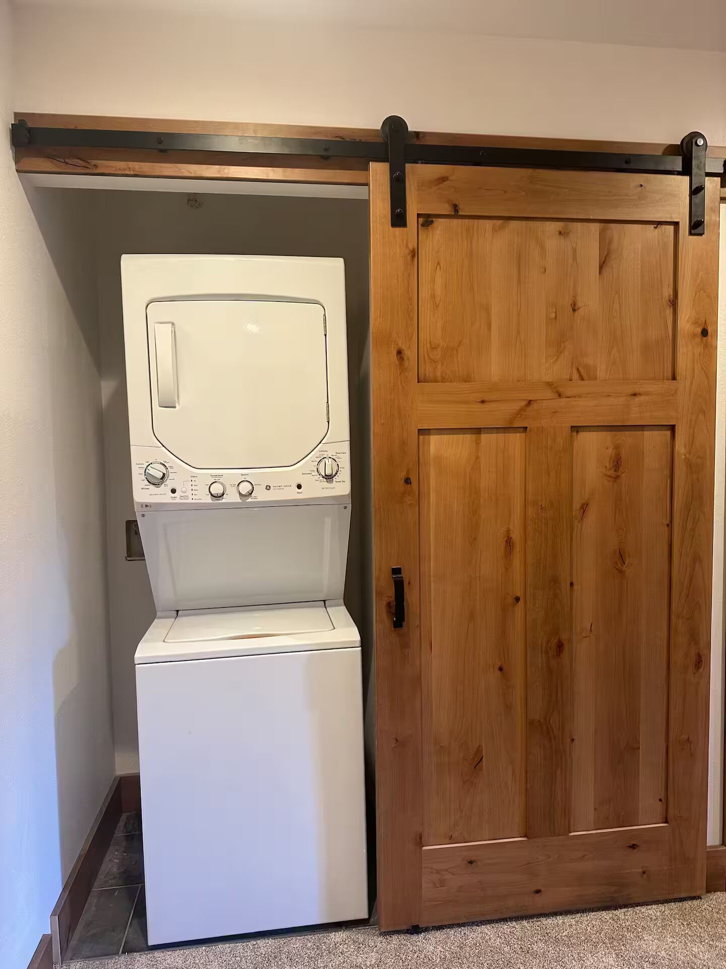 A laundry room with a front-loading washer and dryer, a wooden door, and a metal track system above the door.