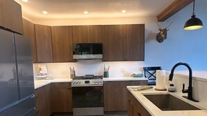 Een moderne keuken met houten kastjes, een roestvrijstalen koelkast, een inbouwoven en een spoelbak met een zwarte kraan.