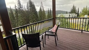 Een overdekt terras buiten met twee stoelen en een tafel, met uitzicht op een bebost landschap.