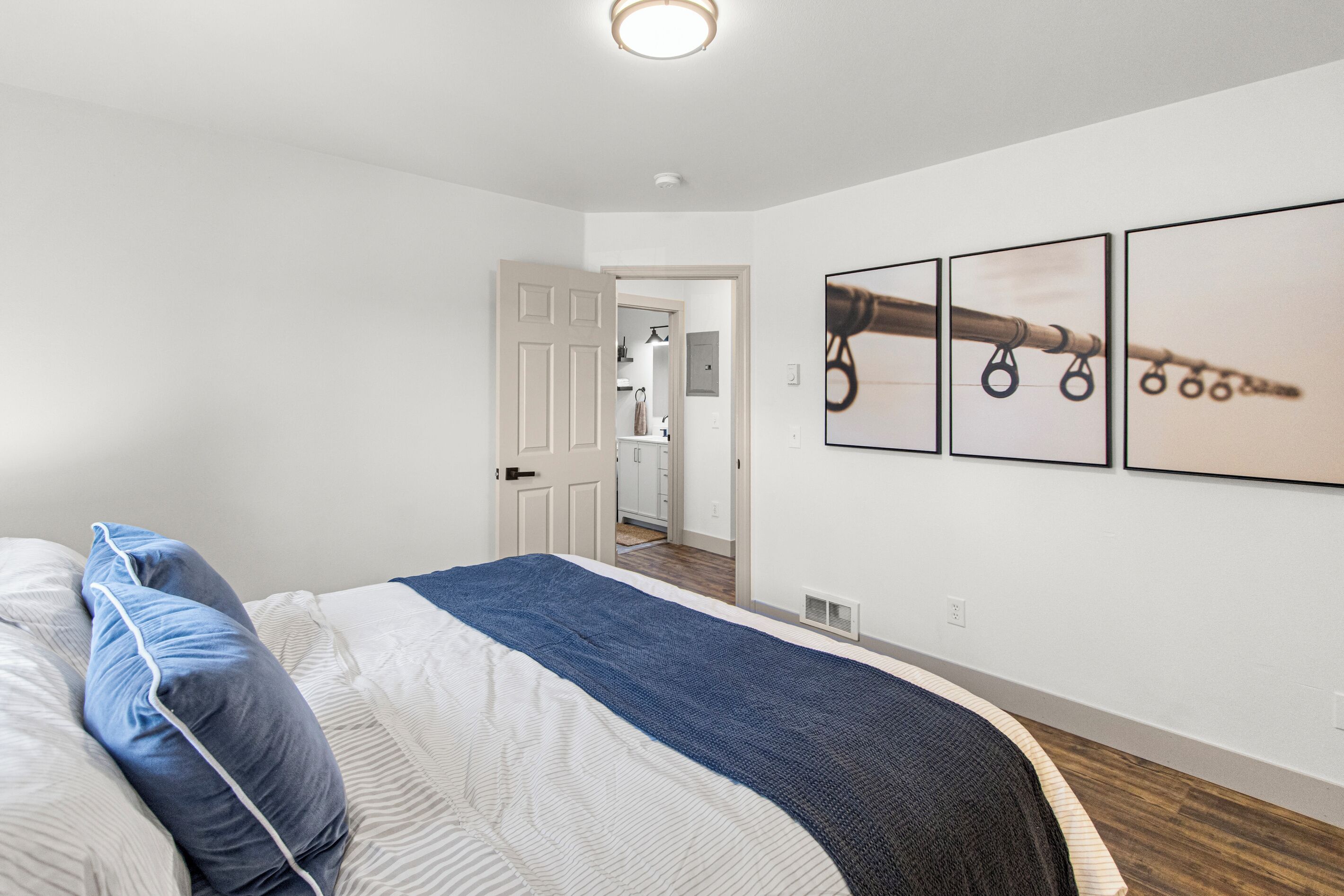 Un dormitorio con cama, una puerta que da a un baño y tres cuadros en la pared.