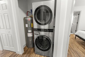 Pequeña y moderna lavandería con lavadora y secadora integradas, calentador de agua y puerta que da a otra habitación.
