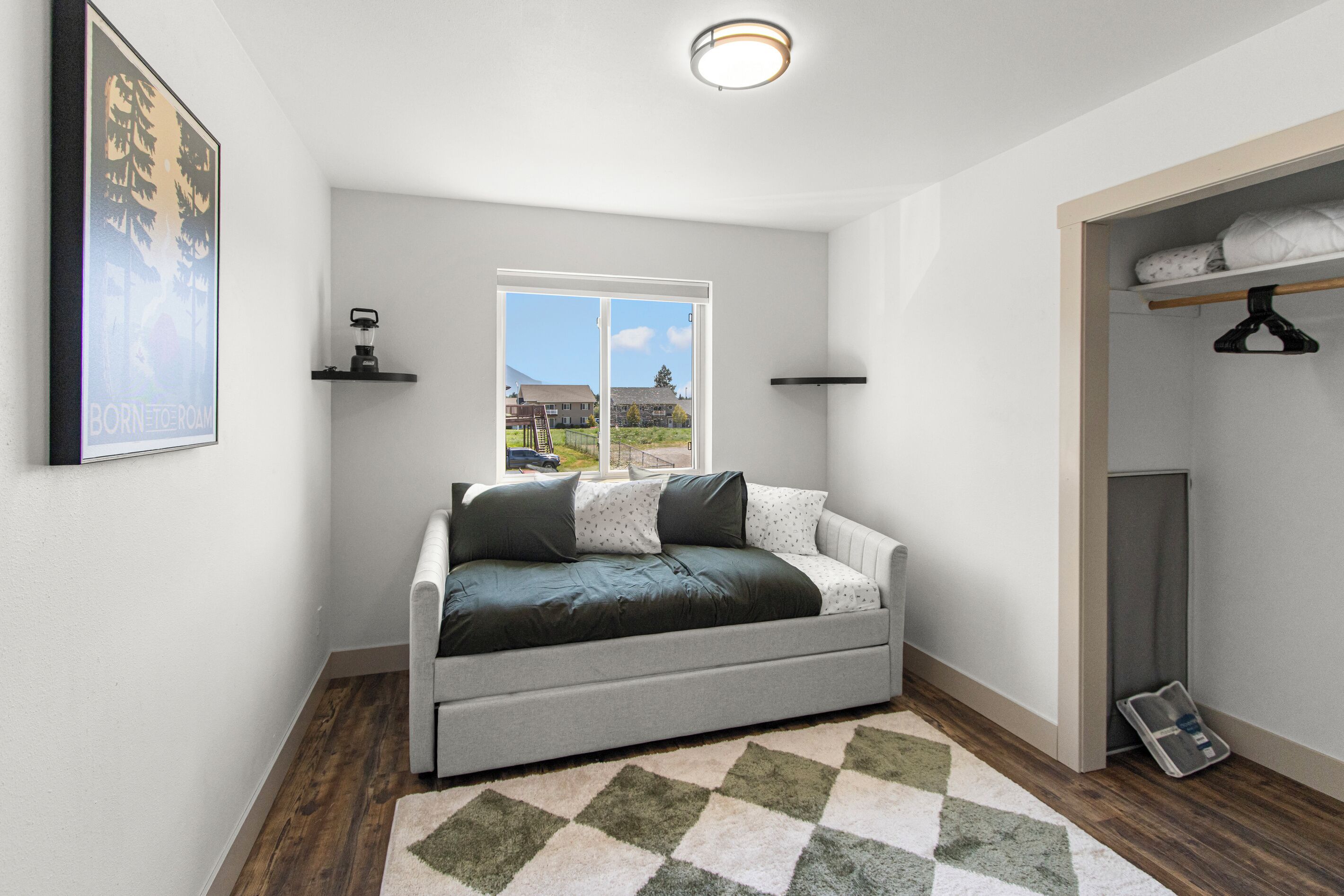 Ein modernes Schlafzimmer mit Schlafsofa, Fenster mit Aussicht, Kleiderhaken und einem gerahmten Bild an der Wand.