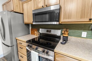Una cocina con armarios de madera, un refrigerador de acero inoxidable, un microondas, un horno y una encimera de granito.